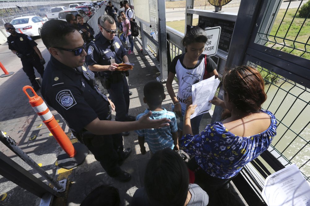 FILE - In this July 17, 2019, file photo, a United States Customs and Border Protection Officer checks the documents of migrants before being taken to apply for asylum in the United States, on International Bridge 1 in Nuevo Laredo, Mexico. On Wednesday, July 24, 2019, a federal judge in San Francisco will hear arguments in a challenge to the new Trump Administration policy that requires asylum-seekers who cross through a third country headed to the U.S. to first apply for protection in that other country. The lawsuit was brought by the American Civil Liberties Union, Southern Poverty Law Center, and Center for Constitutional Rights as they seek a temporary restraining order to block the plan. (AP Photo/Marco Ugarte, File