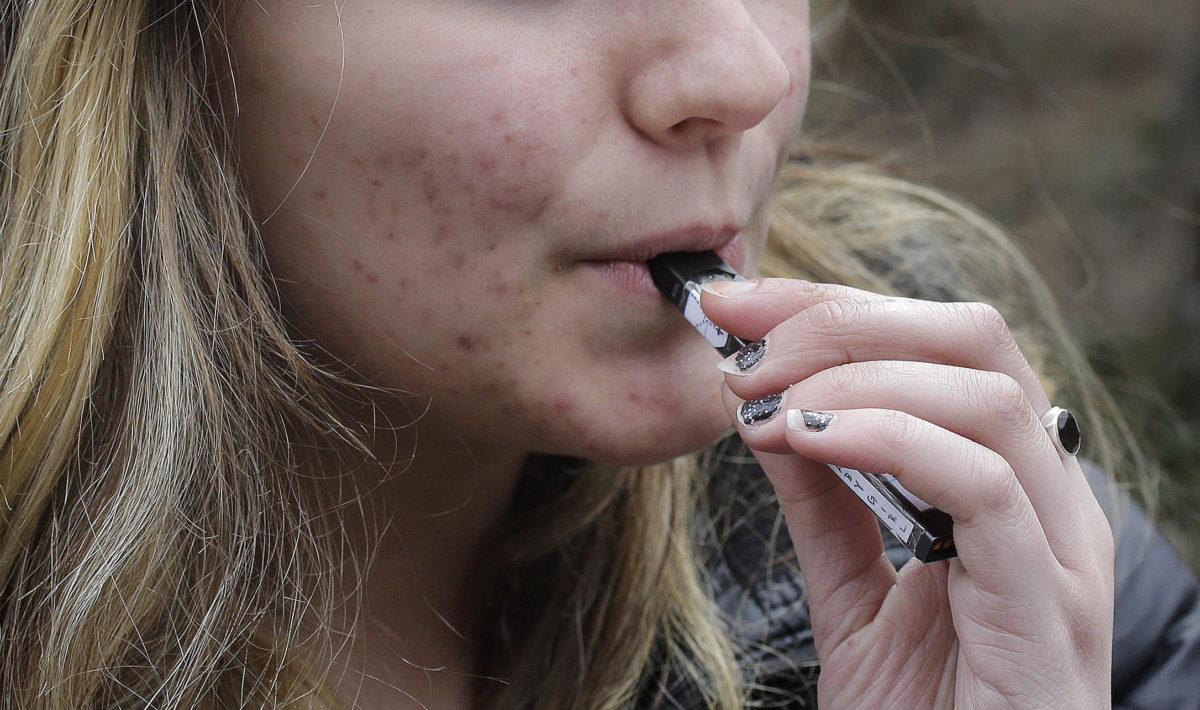 In this Wednesday, April 11, 2018 photo, an unidentified 15-year-old high school student uses a vaping device near the school's campus in Cambridge, Mass. Health and education officials across the country are raising alarms over wide underage use of e-cigarettes and other vaping products. The devices heat liquid into an inhalable vapor that's sold in sugary flavors like mango and mint — and often with the addictive drug nicotine. (AP Photo/Steven Senne)